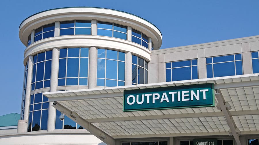 A white medical building labeled outpatient provides various types of IOP and PHP substance addiction treatment.
