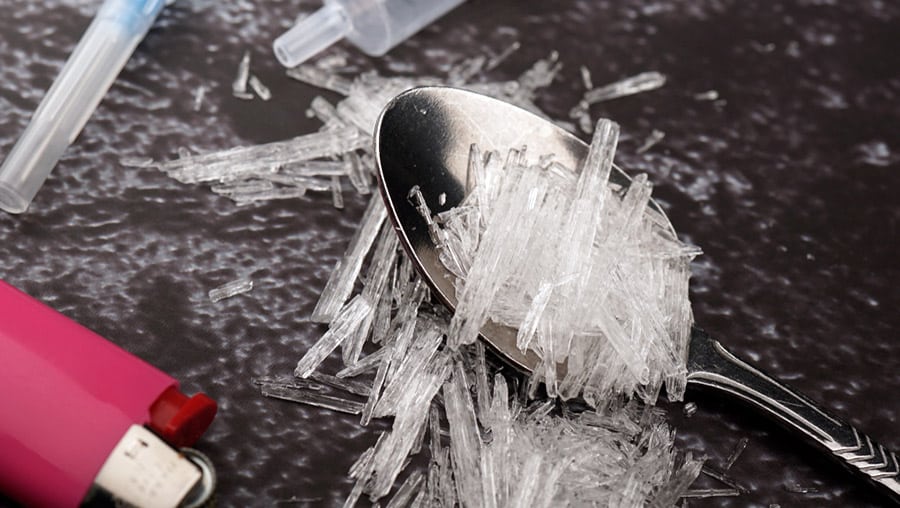 A spoon of crystal meth particles is lying on a dark surface next to a lighter and syringe possibly from the Colorado Library Meth contaminated location. 