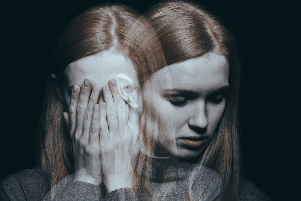 Red haired woman suffering from dual diagnosis - out of focus holding her head in her hands with her shadow self turning and looking down 