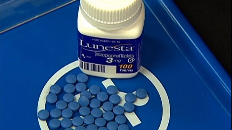 A bottle of 3mg Lunesta medication is next to a handful of blue Lunesta pills on a blue pharmacy tray.

