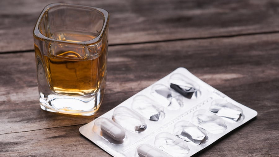 A glass of alcohol sits next to a pack of medication tablets represents the effects of drinking while on antibiotics. 