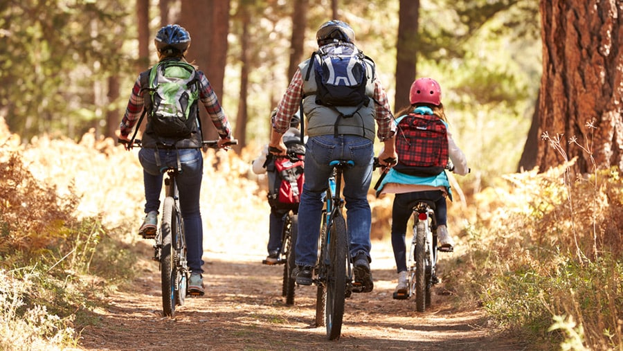 A group of four young people with helmets and a backpack, riding bikes on a trail outdoors represents teen health and wellness. 