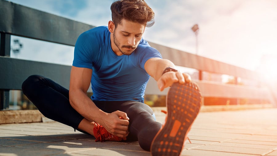 A young man in a blue shirt is on the floor stretching his legs before a run, participates in exercise for addiction recovery. 