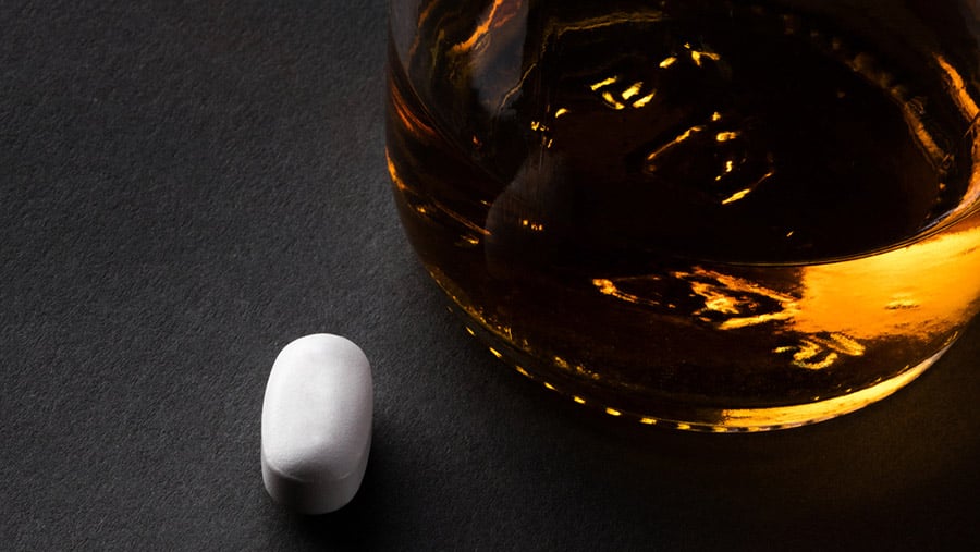 A glass of liquor sitting next to a pain killer medication represents effects of mixing ibuprofen and alcohol. 