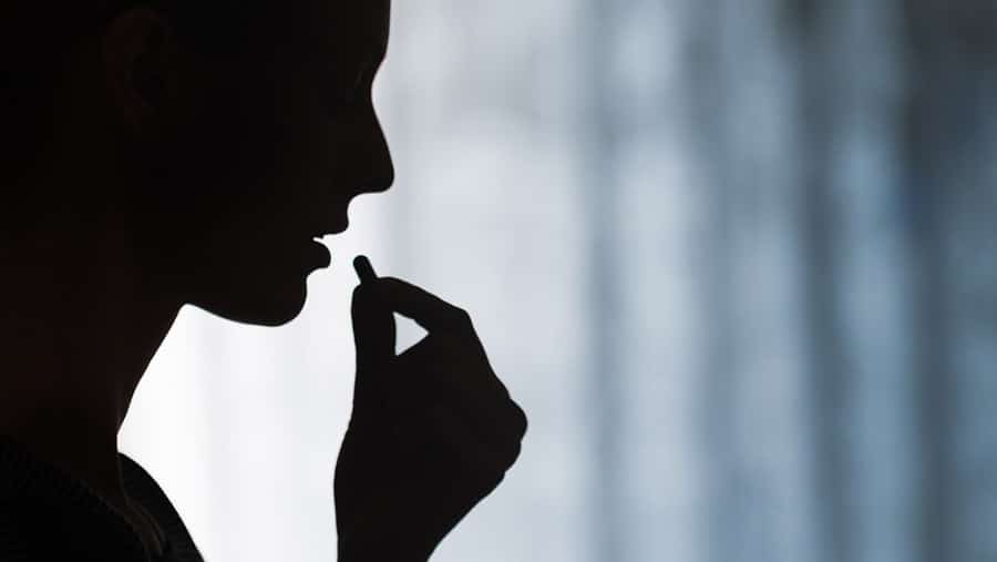 A silhouette of a person raising a pill to their mouth as they wonder what are the long term effects of opioids.  