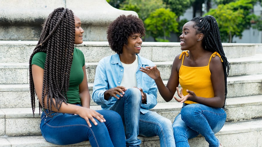 Three young persons of color sitting on a set of stairs outside discussing substance abuse treatment in communities of color.