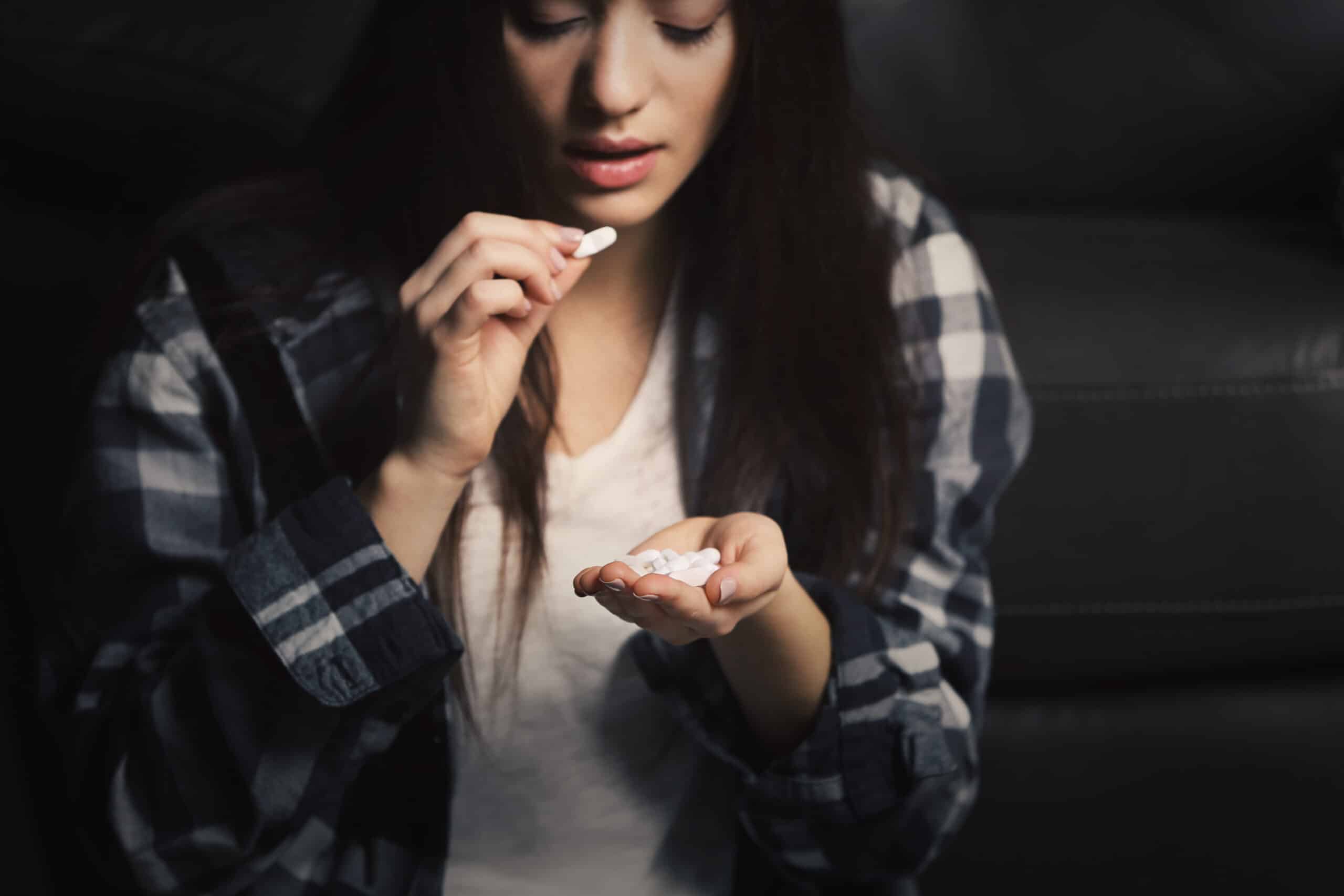 Young female in plaid shirt raising her hand to take a white klonopin pill while in the other hand holding the remaining white pills represents her klonopin addiction.