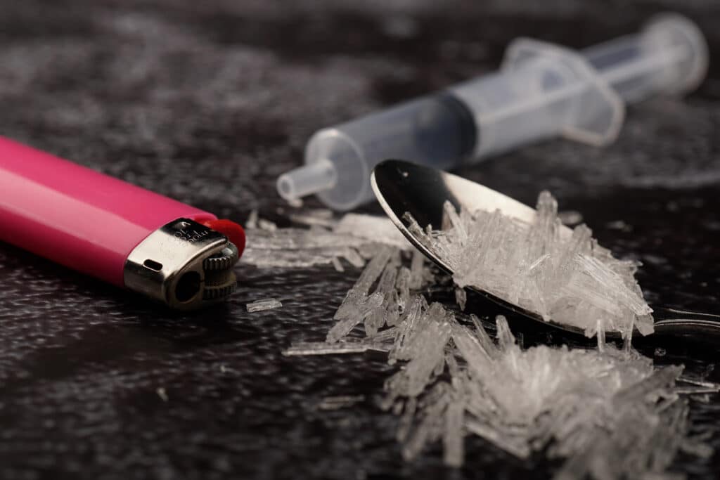 A red lighter, syringe and spoon filled with crystal meth lays on a black surface. How long does meth stay in your system?