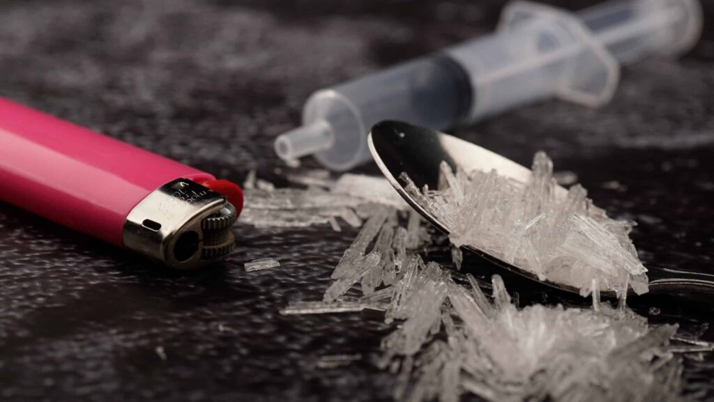 A red lighter, syringe and spoon filled with crystal meth lays on a black surface. How long does meth stay in your system?