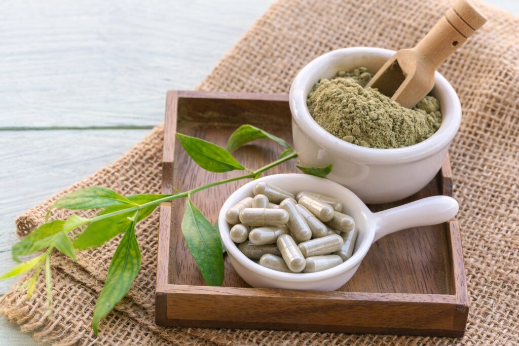Small bowls of powdered kratom and kratom in pill form sit on a wooden tray with a kratom leaf. This invokes the question of is Kratom legal in Ohio.