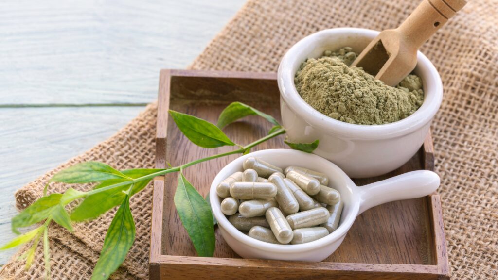 Small bowls of powdered kratom and kratom in pill form sit on a wooden tray with a kratom leaf. This invokes the question of is Kratom legal in Ohio.