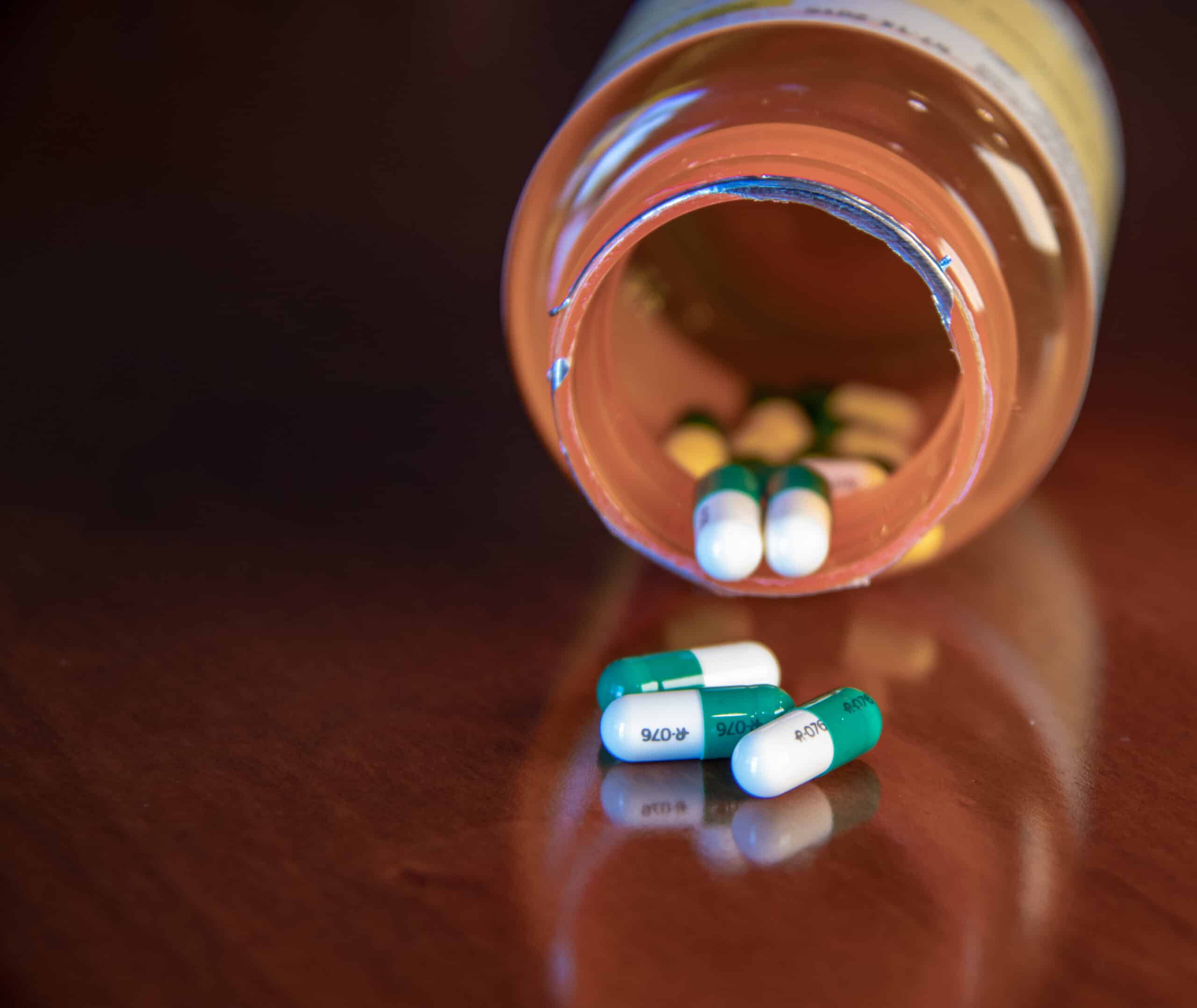 A tipped over pill bottle on a wooden table with green and white pills spilled out. It represents Restoril vs Ambien, both drugs to treat insomnia.