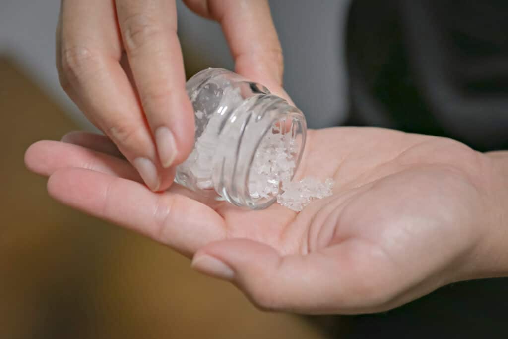 A person wondering what is flakka, pours crystal white bath salts out from a small glass jar onto their hand.