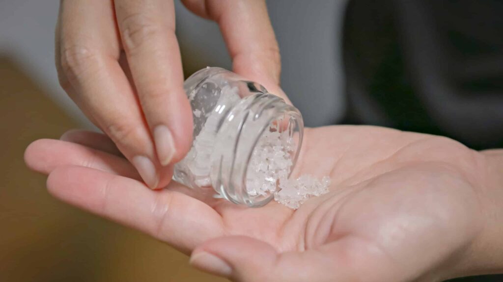 A person wondering what is flakka, pours crystal white bath salts out from a small glass jar onto their hand.