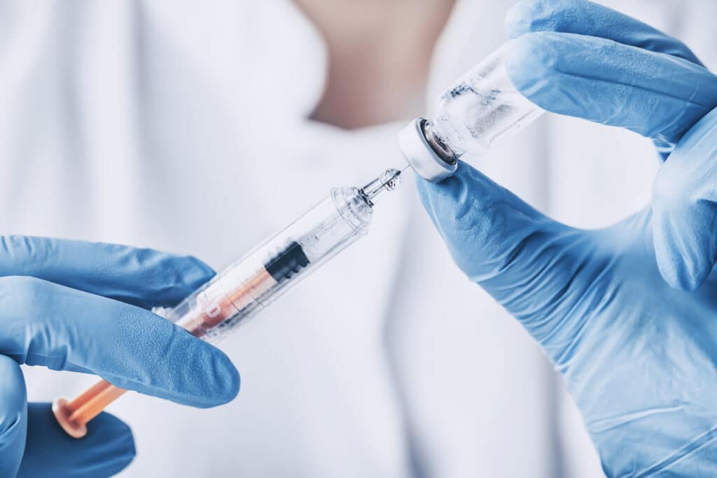 A close up of a medical professionals hands in blue gloves retrieving Vivitrol liquid into a syringe, while answering the question of how long does vivitrol last in the body.