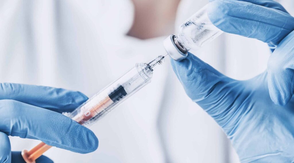 A close up of a medical professionals hands in blue gloves retrieving Vivitrol liquid into a syringe, while answering the question of how long does vivitrol last in the body.