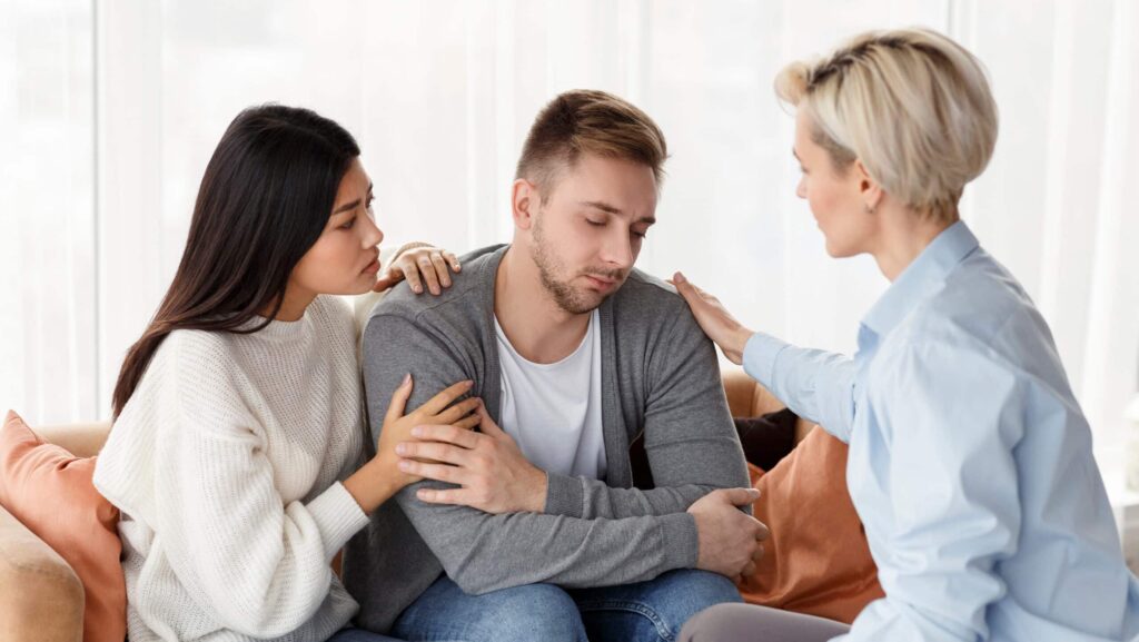 A young man with a drug addiction being consoled by two female friends represents the difference between enabling an addict and supporting an addict.
