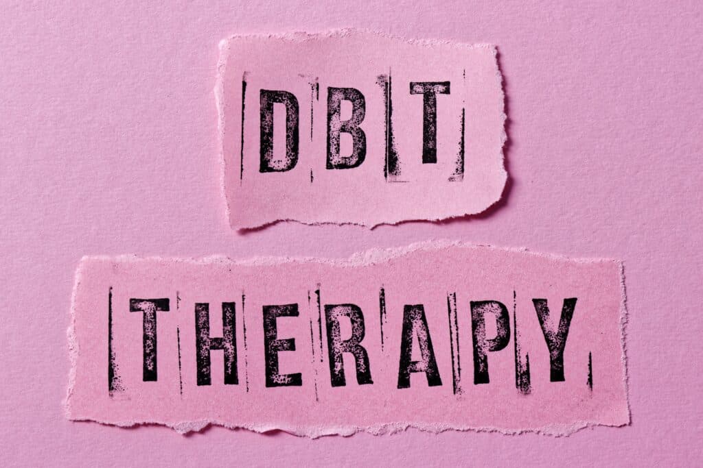 A pink background with the word DBT Therapy is printed in black represents the six main points of dialectical behavior therapy.