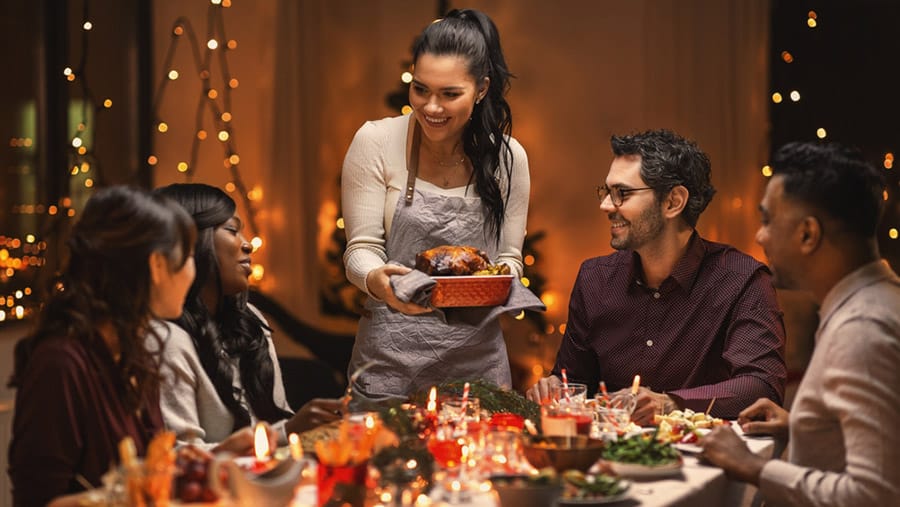 Dark haired woman serving turkey during sober holiday to table of friends