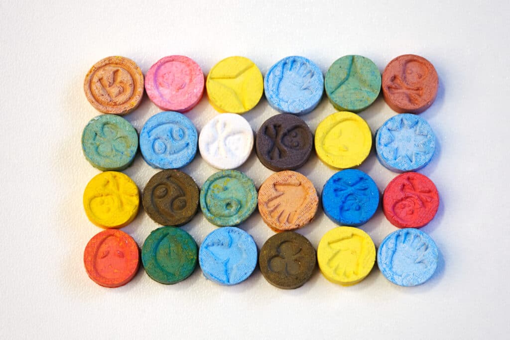 Various rows and columns of colorful ecstasy tablets lay on a table. The formulation of these tablets bring up the question of how long ecstasy stays in your system.