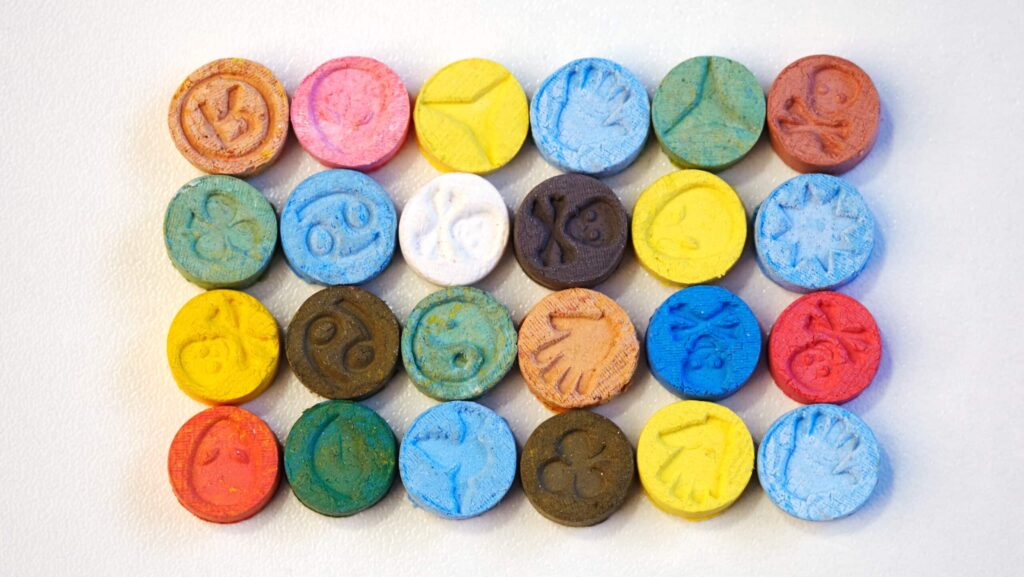 Various rows and columns of colorful ecstasy tablets lay on a table. The formulation of these tablets bring up the question of how long ecstasy stays in your system.