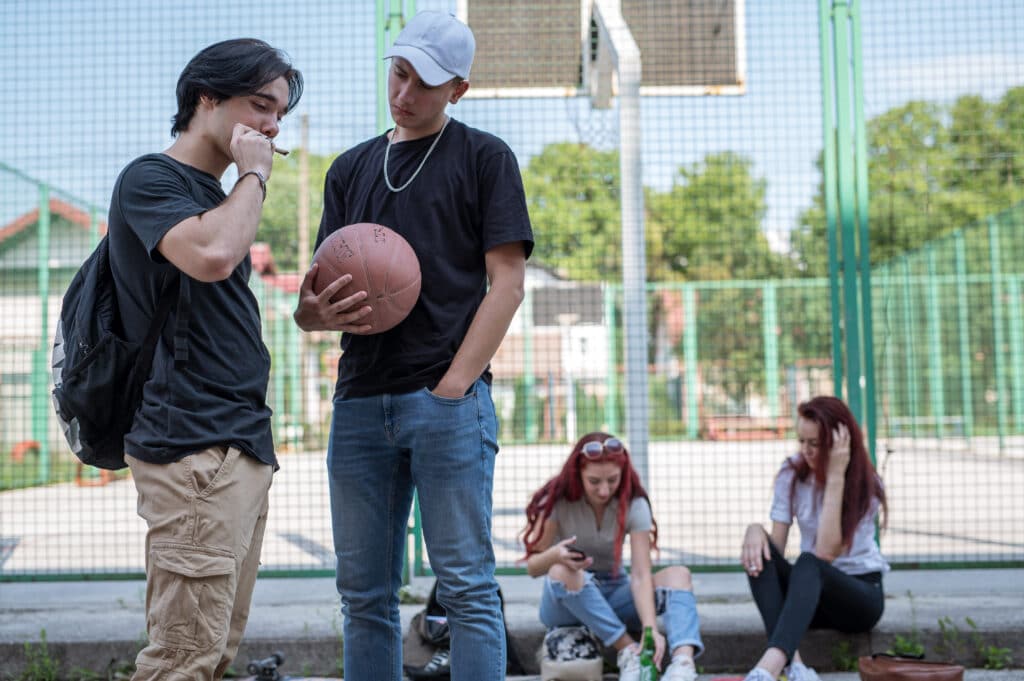 Four students, 2 girls and 2 boys, hanging out on school grounds smoking and considering the benefits of quitting weed.