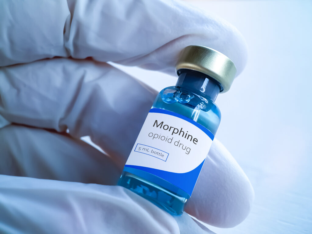 A person in purple gloves is holding a small bottle of morphine that represents how long the substance will stay in the body.