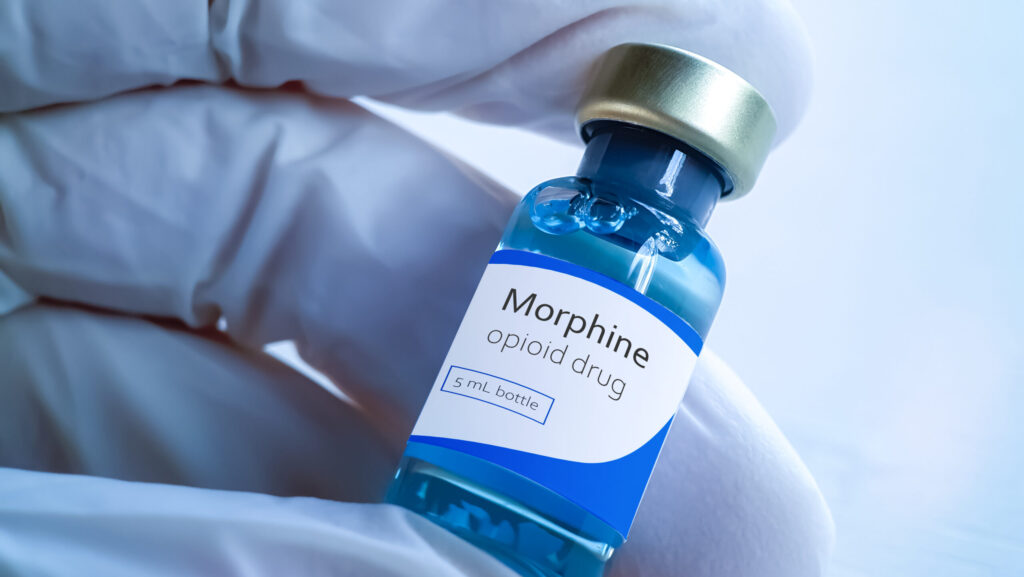 A person in purple gloves is holding a small bottle of morphine that represents how long the substance will stay in the body.