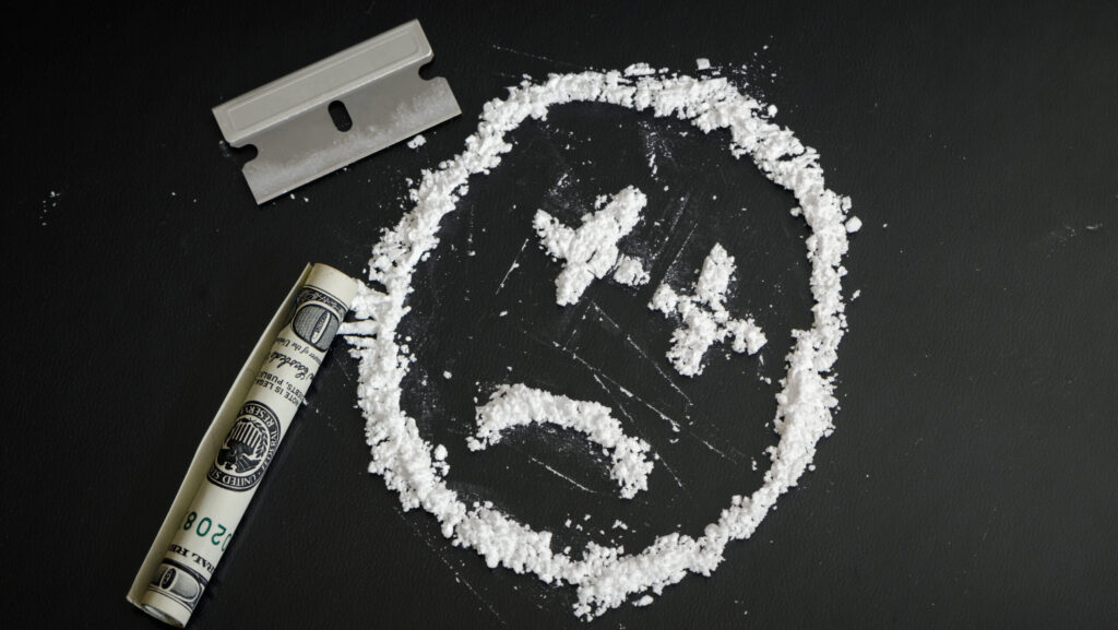 On a black background with a razor and rolled up bill, powdered cocaine is constructed in the shape of a side face. This represents how long cocaine will stay in your urine.