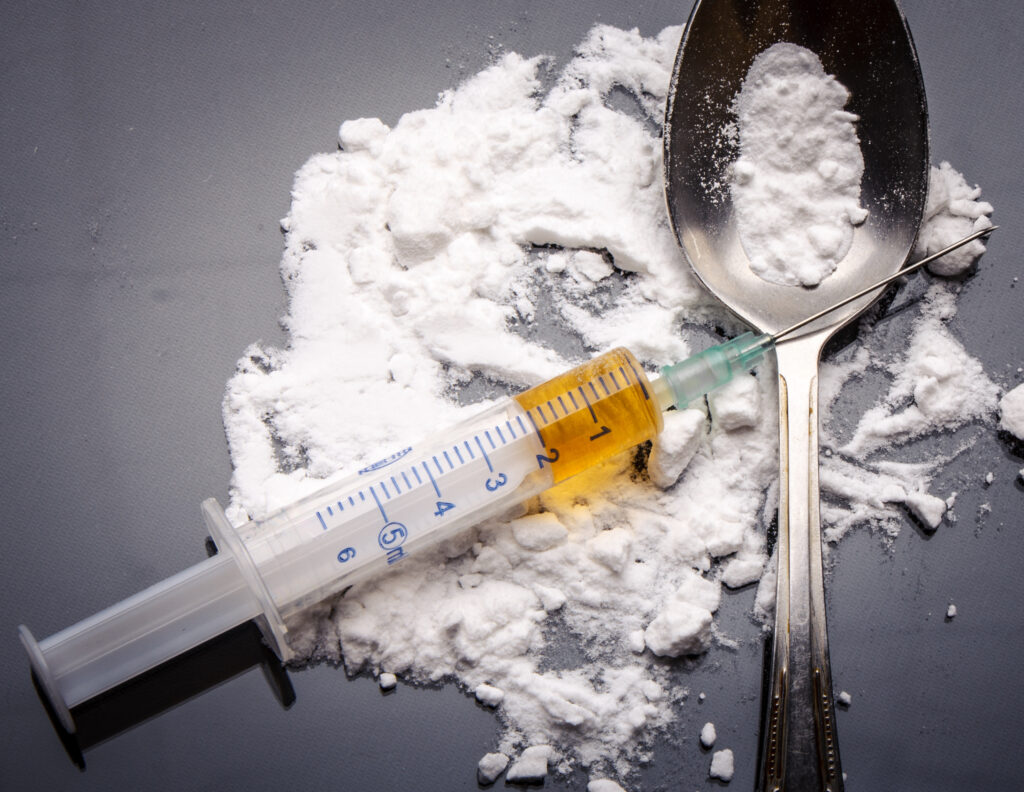 A pile of heroin is spread out on the tablet with a filled syringe and spoon represents the question of how long a heroin high lasts.