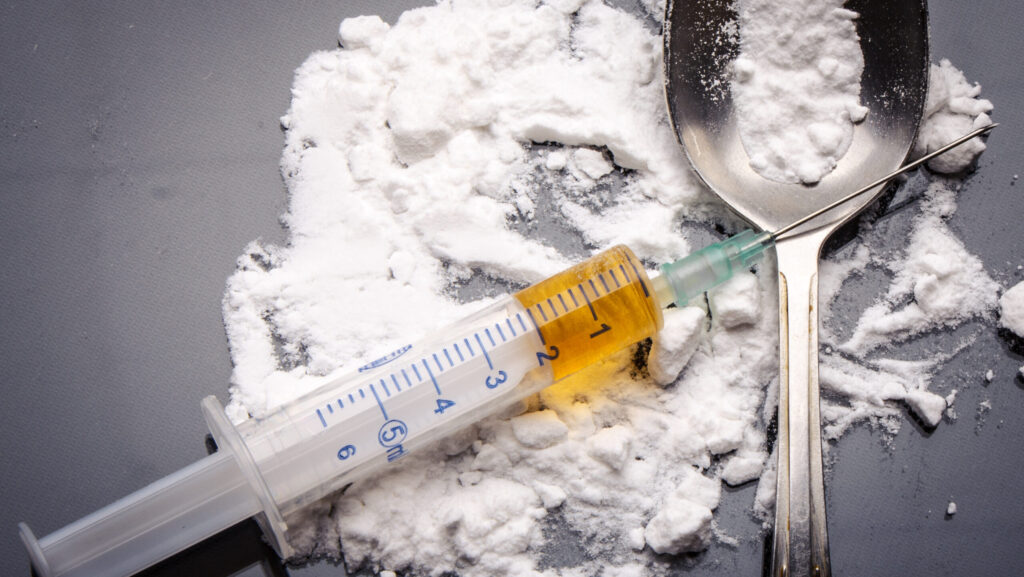 A pile of heroin is spread out on the tablet with a filled syringe and spoon represents the question of how long a heroin high lasts.