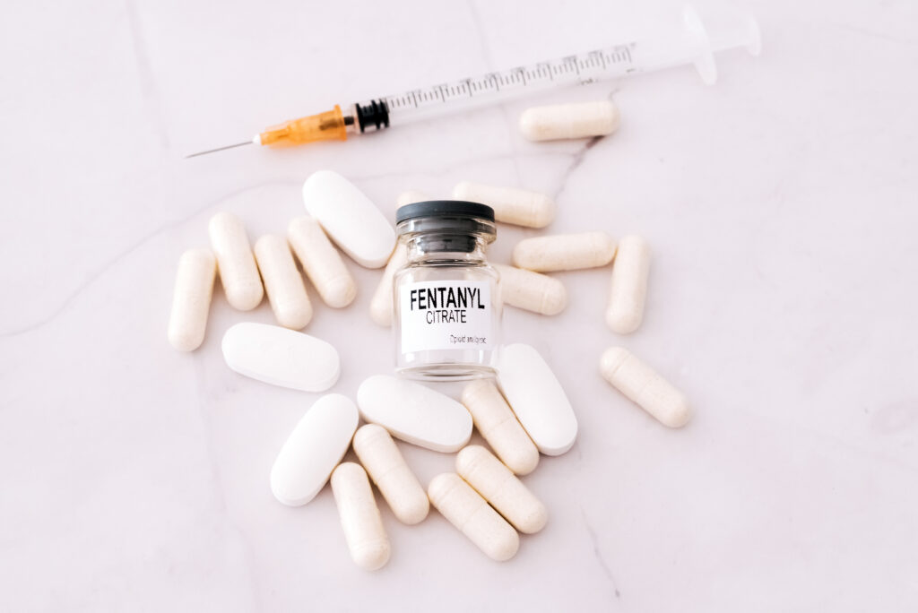 White pills, a syringe and a vile labeled fentanyl citrate lays on a white table. This shows a person may have a fentanyl addiction and may need fentanyl rehab.
