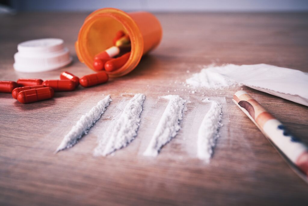 On a table, there is a spilled over bottle of red pills, four lines of cocaine and a rolled up bill. People often question whether or not cocaine is a depressant or stimulant.