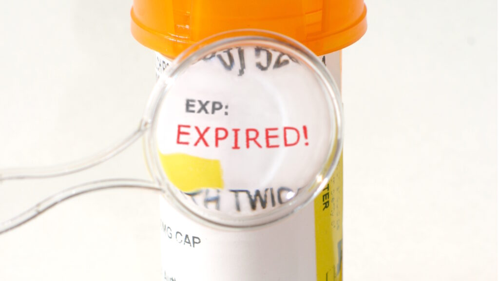 A small magnifying glass zooms in on the word expired on an orange pharmacy pill bottle represents that medications and Adderall expires.