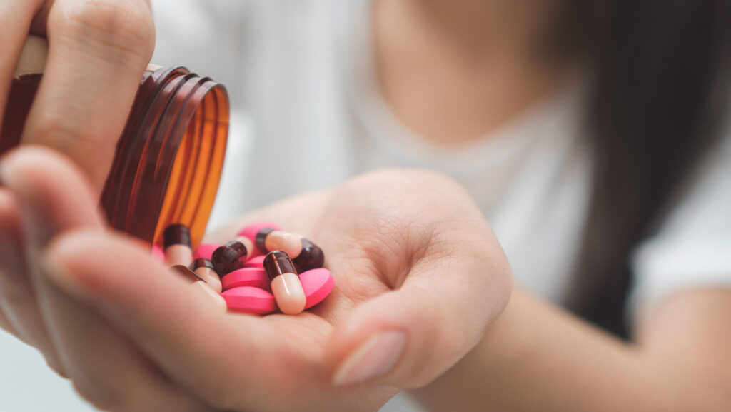 A young woman pours out a bottle of colorful pink Xanax pills and tablets representing an overdose on Xanax.