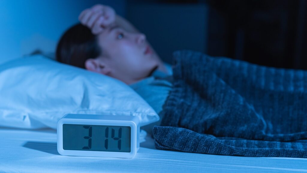 A woman laying awake in bed in front of the clock experiencing insomnia from oxycontin detox.