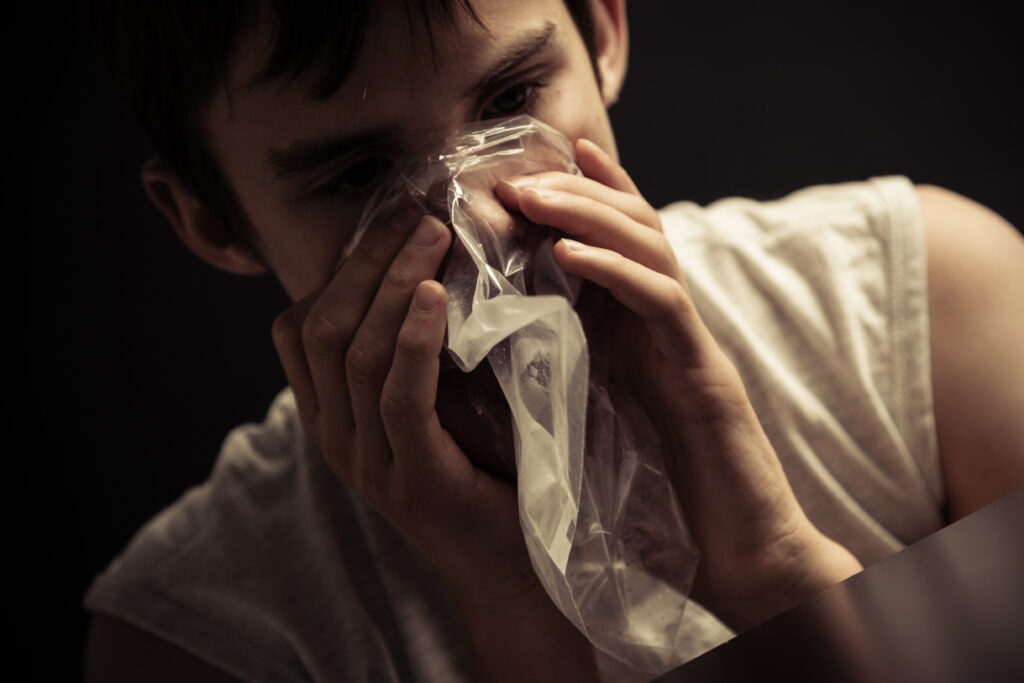 A young man with inhalant use disorder is bagging chemicals from household items with a clear plastic bag.