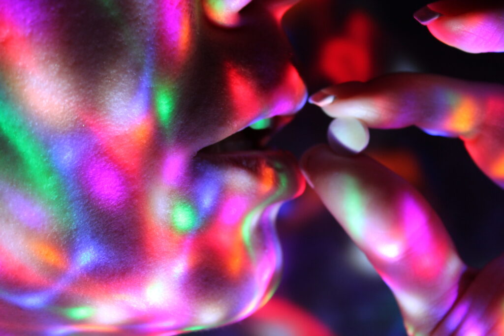 A close up of a young woman holding up a small round ecstasy pill next to her mouth and putting her self at risk for OD on Ecstasy.