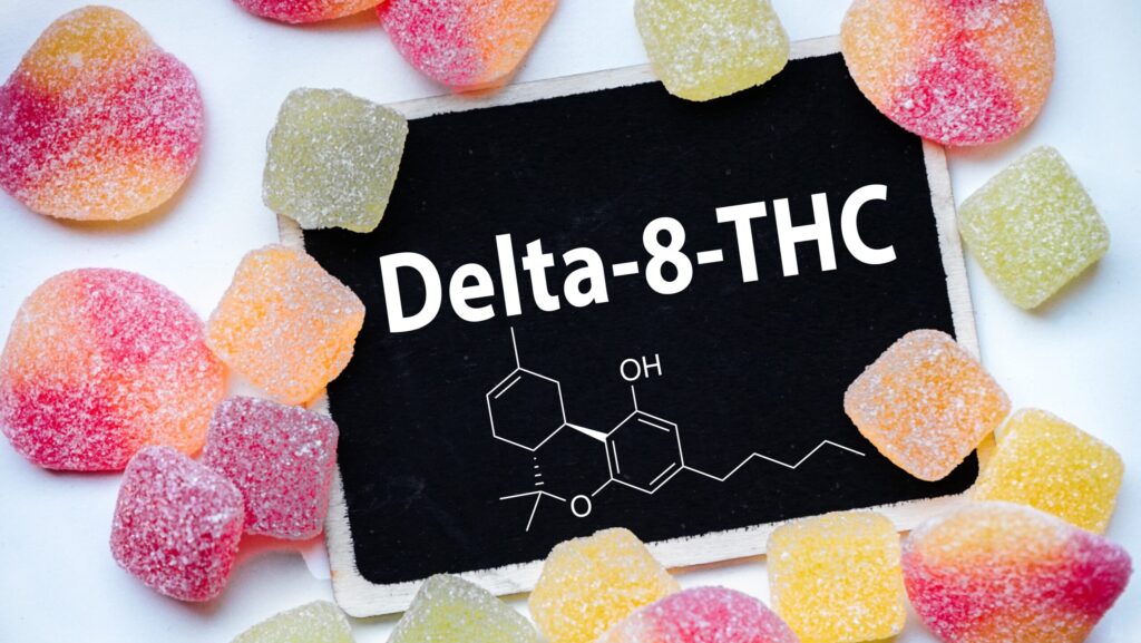 The words Delta 8 THC on a black board is surrounded by various types of gummies represents how long Delta 8 stays in your system.