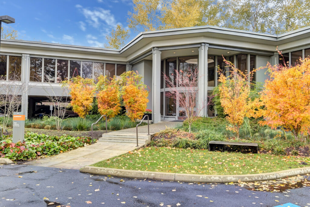 Front of Kaiser Addiction Treatment building. White walls, orange trees and sidewalk with ramp leading to glass doors.