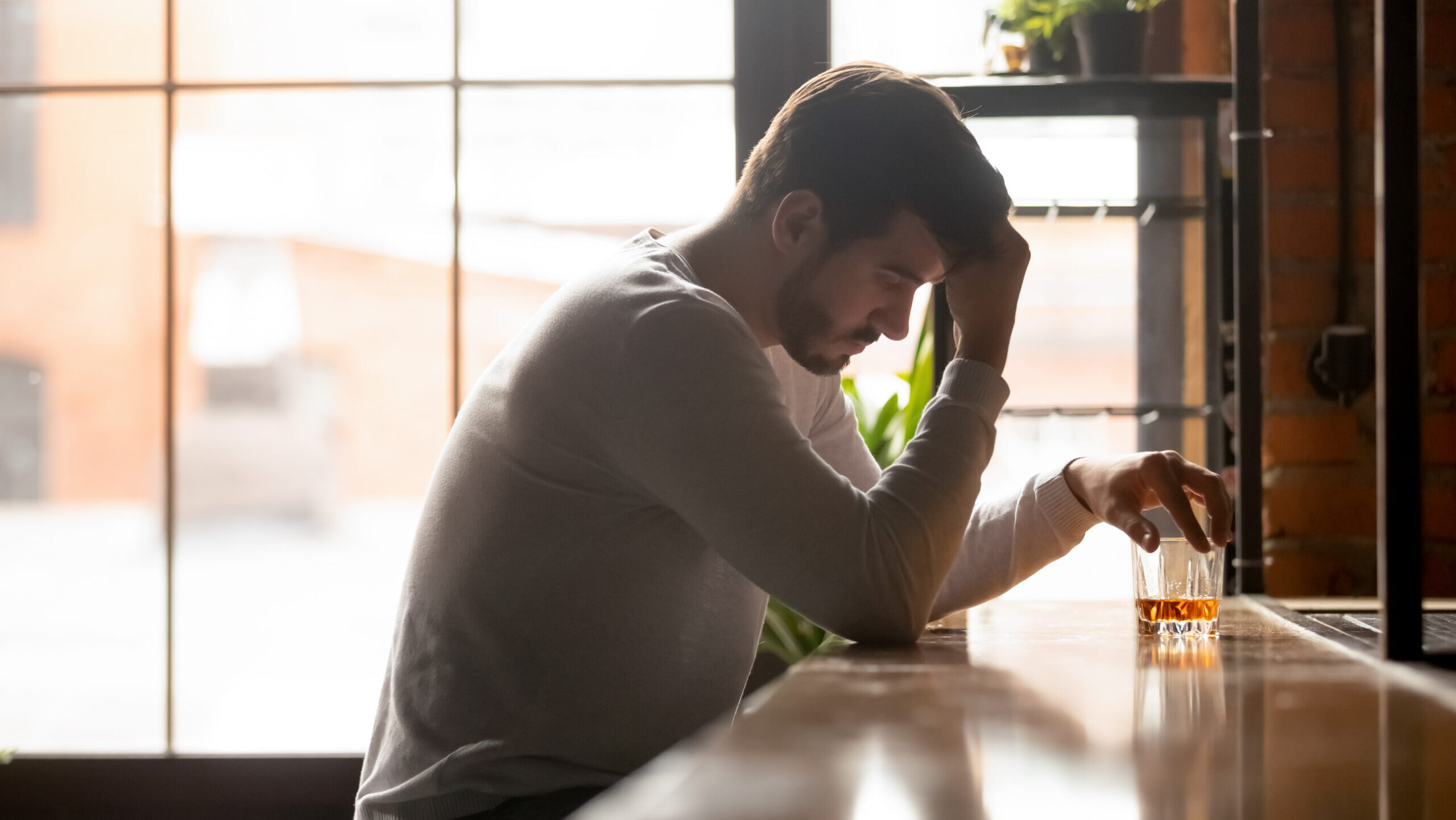 A young man sitting at a bar counter with a drink struggling with alcohol and mental health effects.