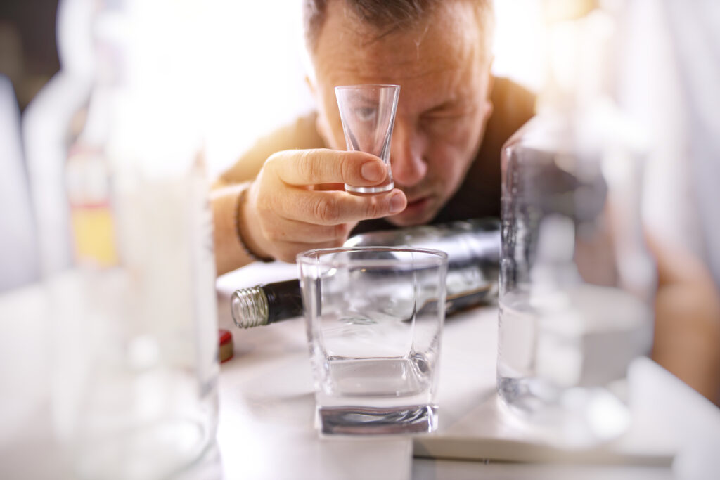 A man holding a shot glass of alcohol wondering if there are drugs to stop alcohol cravings.