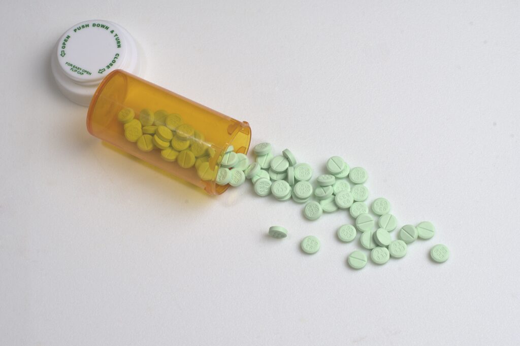 Green pills spilling out from an orange pill container represents Klonopin helping with alcohol withdrawal.