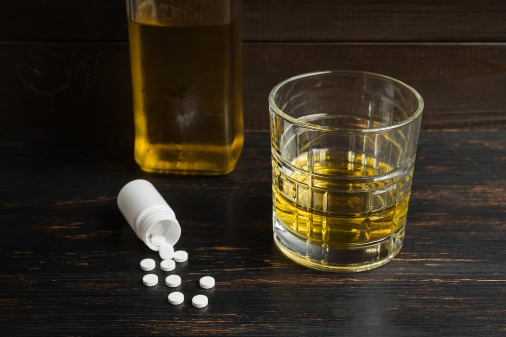 A glass of alcohol and a spilled over bottle of prescription medications represents the relationship with Wellbutrin and alcoholism.