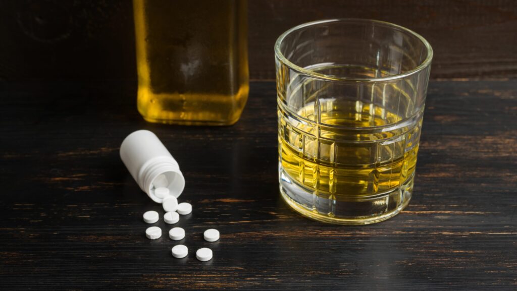 A glass of alcohol and a spilled over bottle of prescription medications represents the relationship with Wellbutrin and alcoholism.