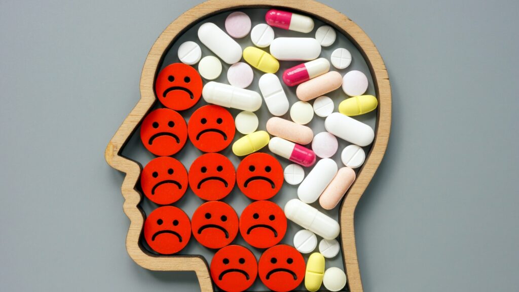 A person's head filled with various pills and frowning faces represents what happens when you drink on antidepressants.
