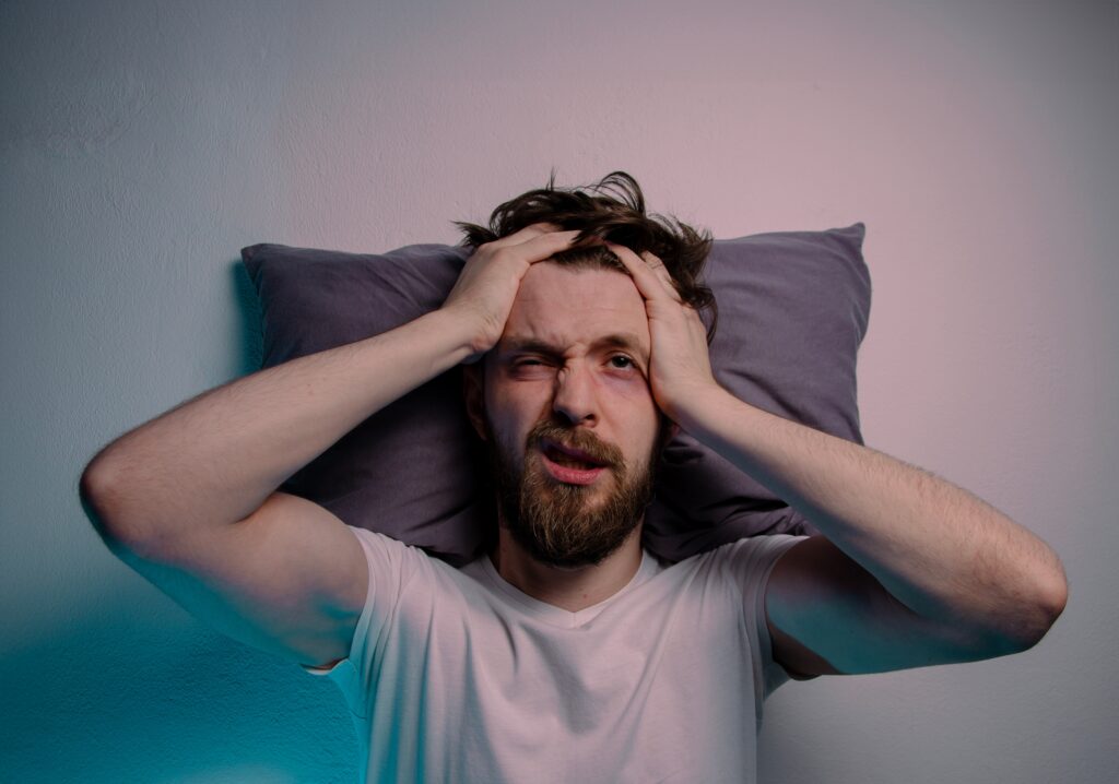 A man laying on a pillow is experiencing hangover symptoms and is wondering how to get rid of hangxiety.