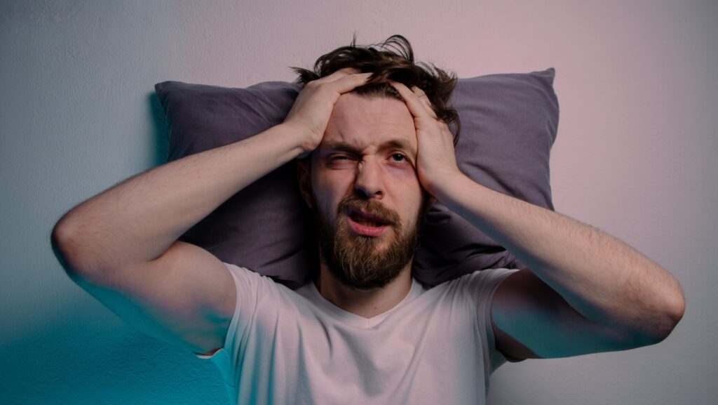 A man laying on a pillow is experiencing hangover symptoms and is wondering how to get rid of hangxiety.