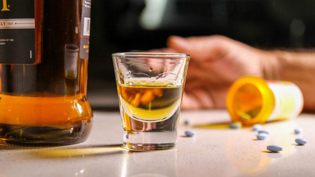 A shot glass of alcohol next to a spill over pill bottle of morphine represents the dangers of mixing morphine and alcohol.