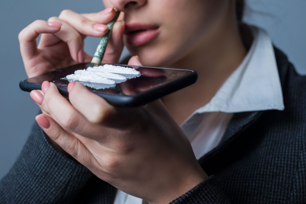 A young women snorting cocaine off her phone anticipating experiencing coke bloat.